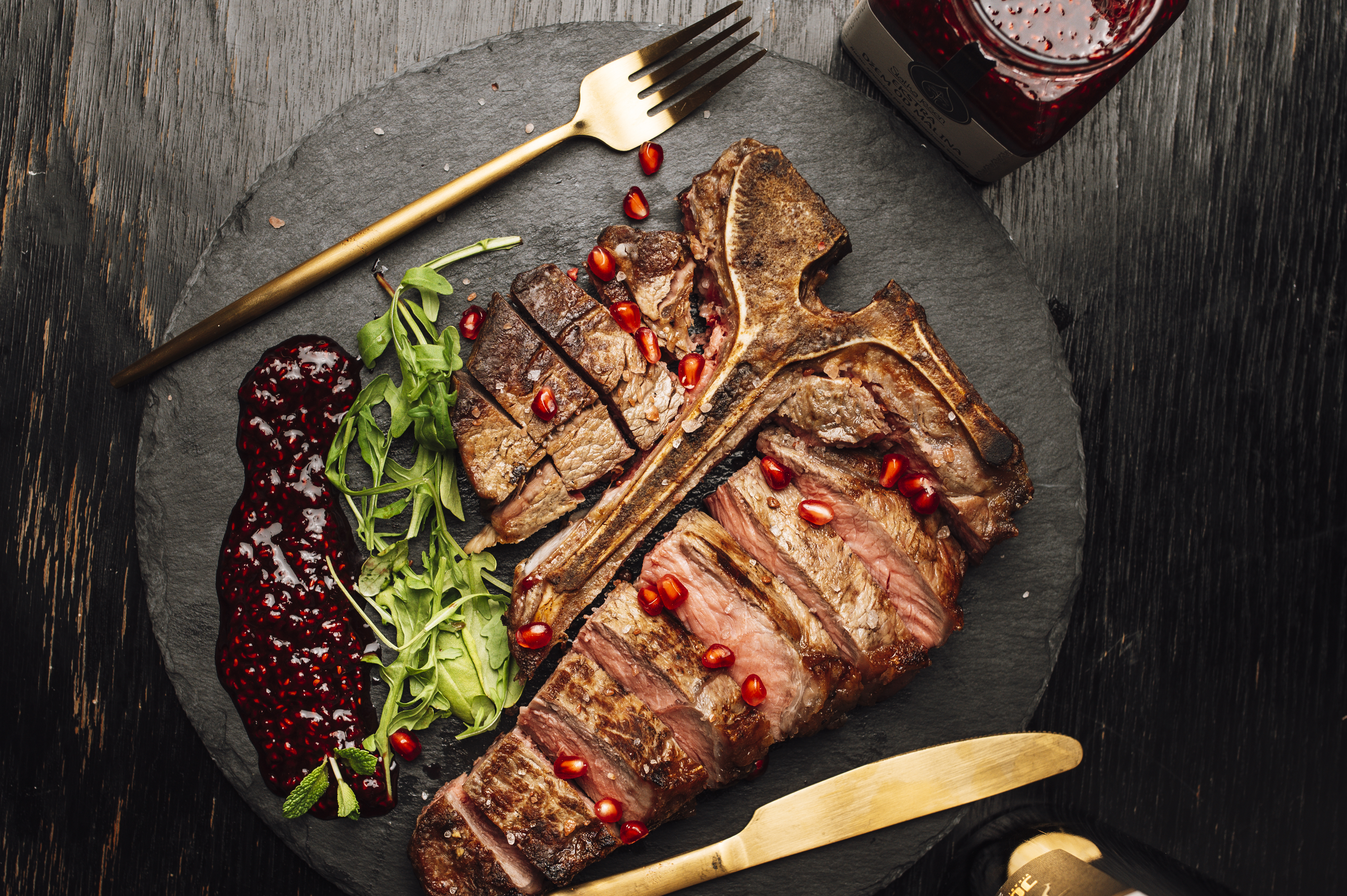 A restaurant-style steak dish plated with greens, sauce, and garnishes on a dark plate